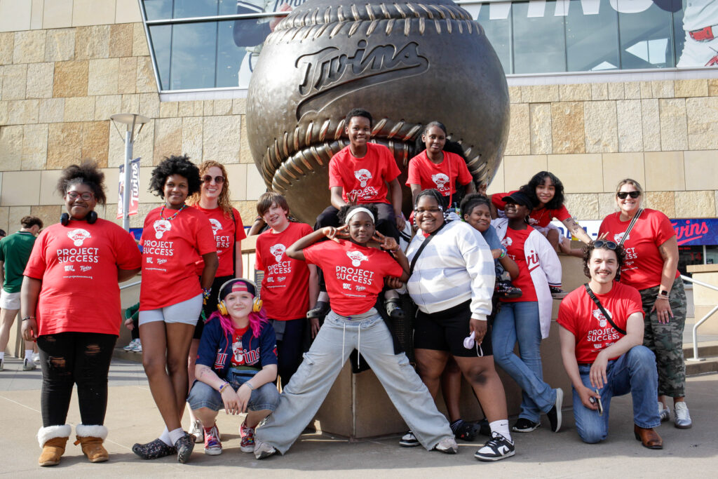 Group of students posing for a picture in front of a large baseball statue.