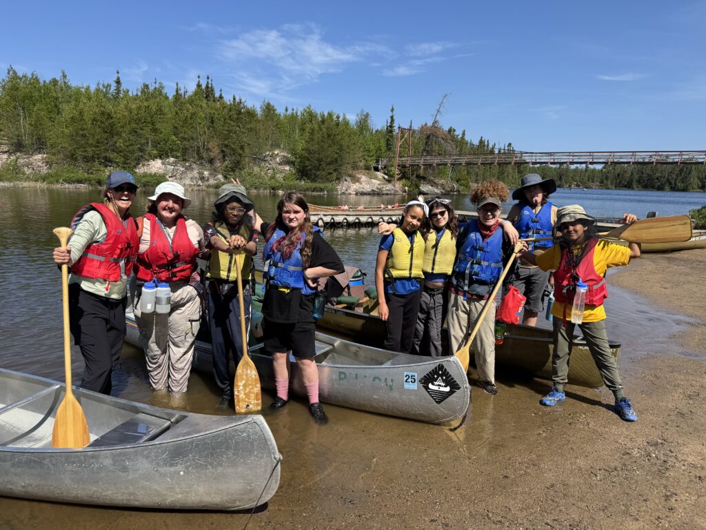 Group of students and leaders smiling in front of their canoes.