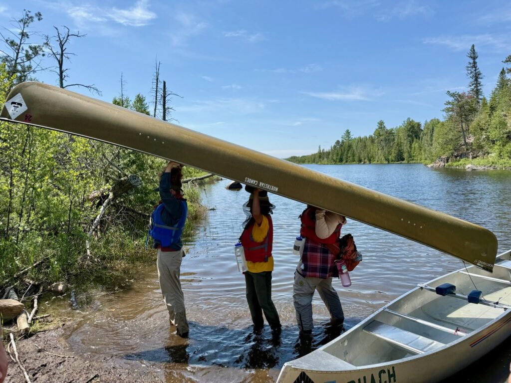 Three students portaging a canoe.