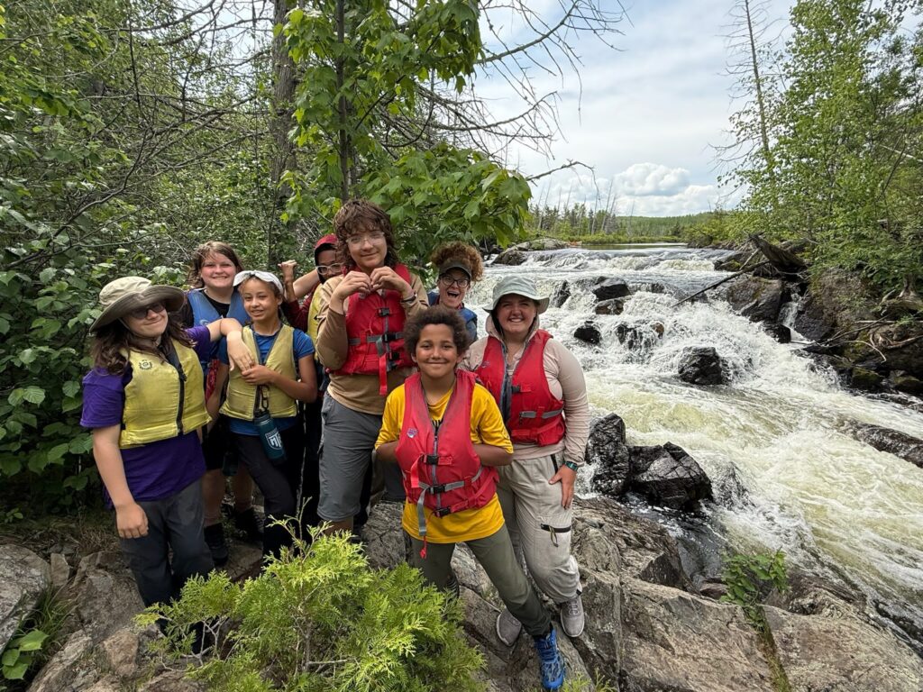 Students in life jackets standing in front of a river.