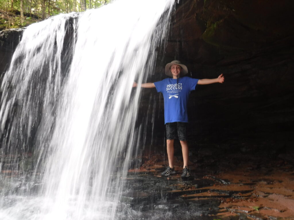 Student with his arms out under a waterfall.