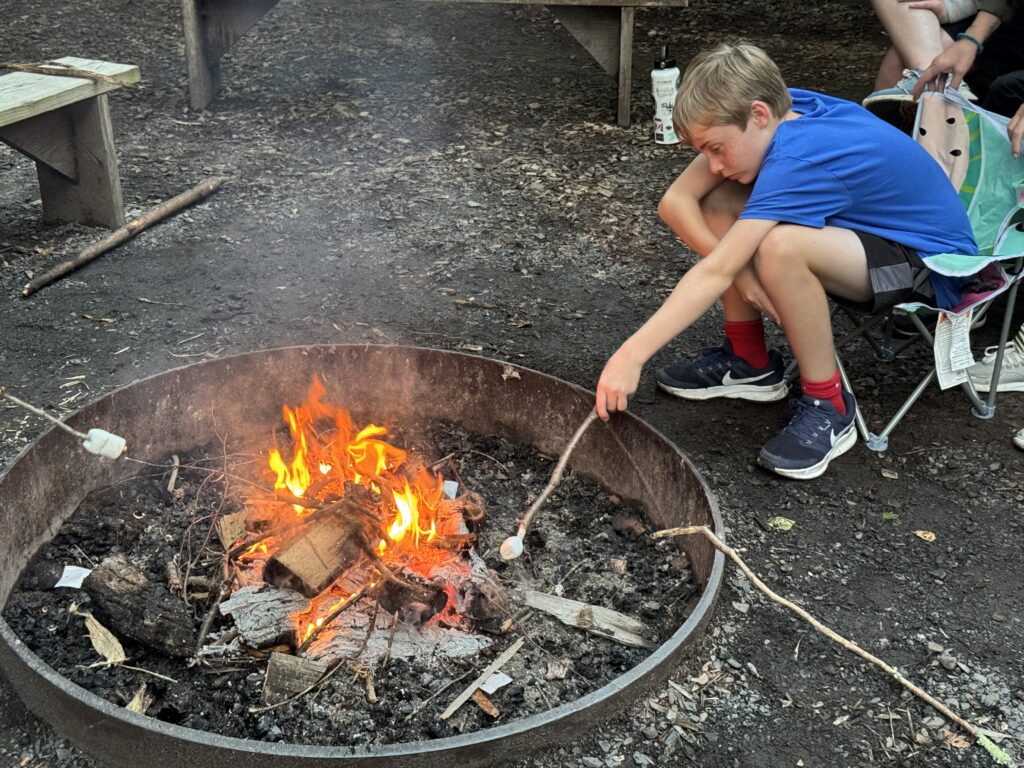 Student roasting marshmallow over campfire.