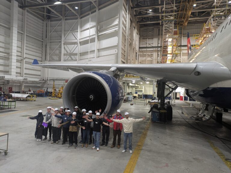 Students with their arms out by a plane engine.